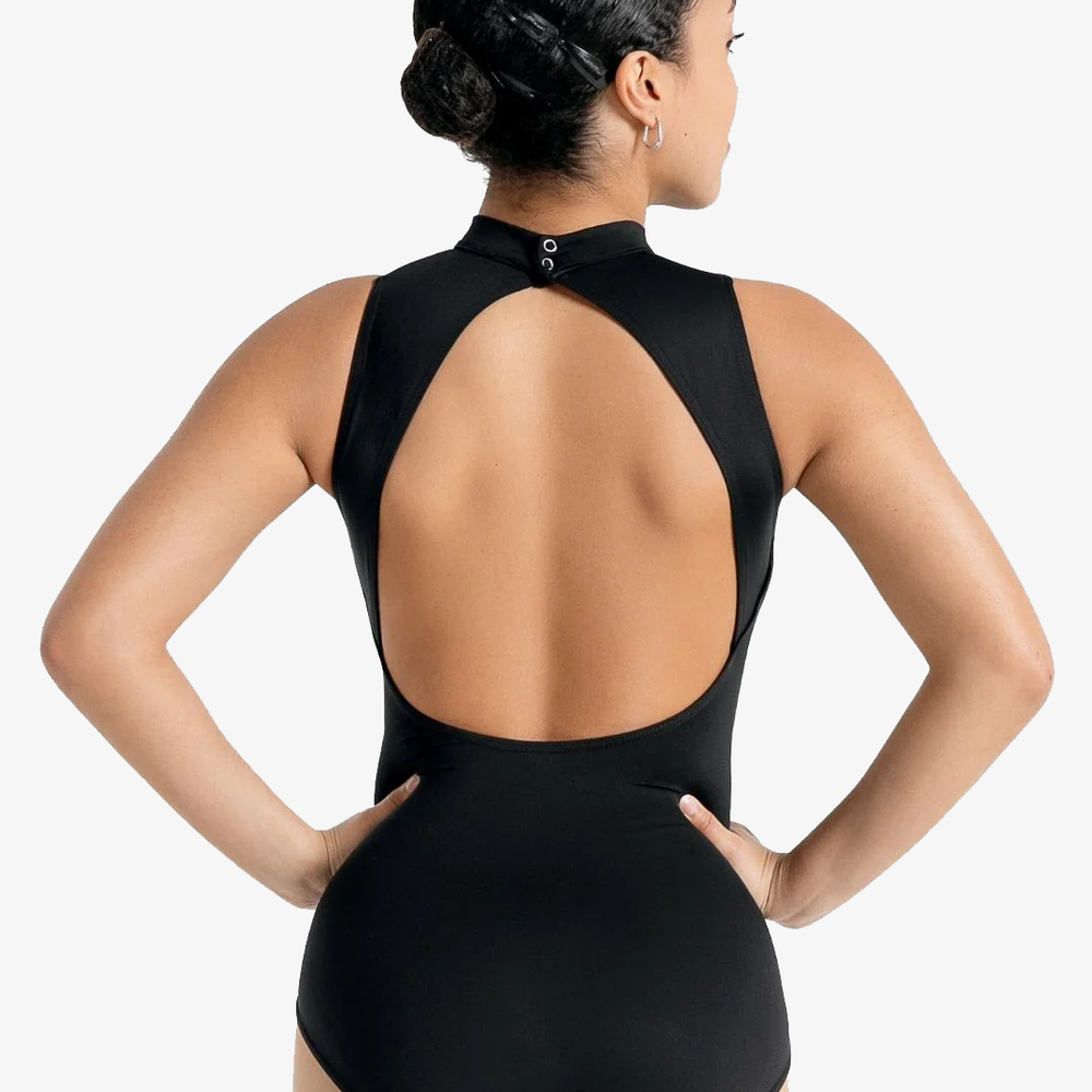 A female stands with her back facing us, hands on hips, black hair pulled back into a bun. The pose showcases the open back and high neck of the black leotard.