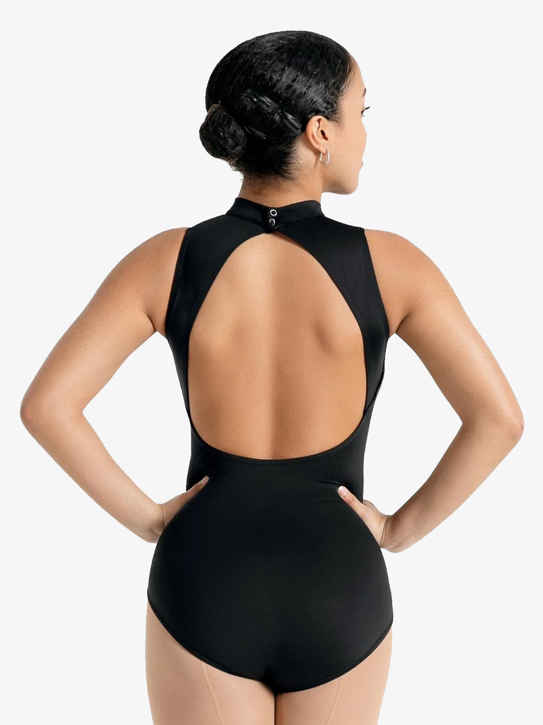 A female stands with her back facing us, hands on hips, black hair pulled back into a bun. The pose showcases the open back and high neck of the black leotard.