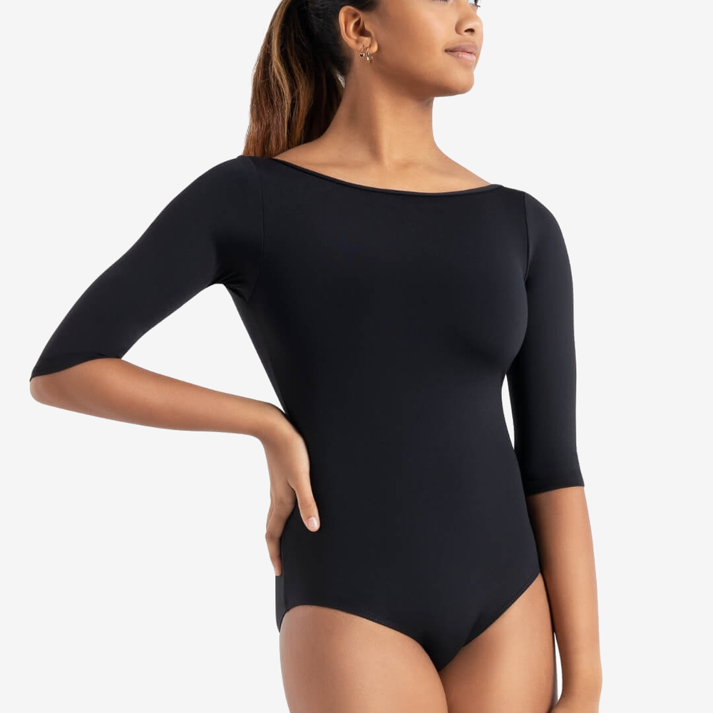 
                      
                        A female dancer with her hand on her hip, wears a 3/4 sleeve, black, boatneck leotard. She has her hair pulled back into a ponytail and stares off to the side with a happy, calm expression.
                      
                    