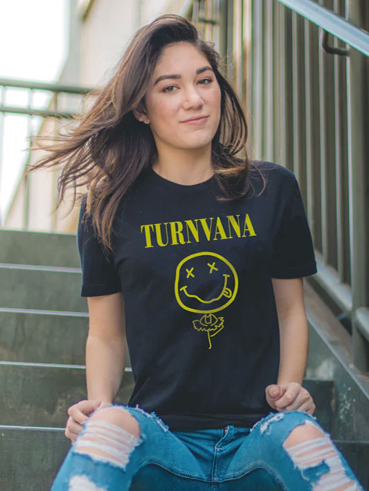 A young woman with long, flowing hair sits on outdoor steps, wearing a black T-shirt with the word 