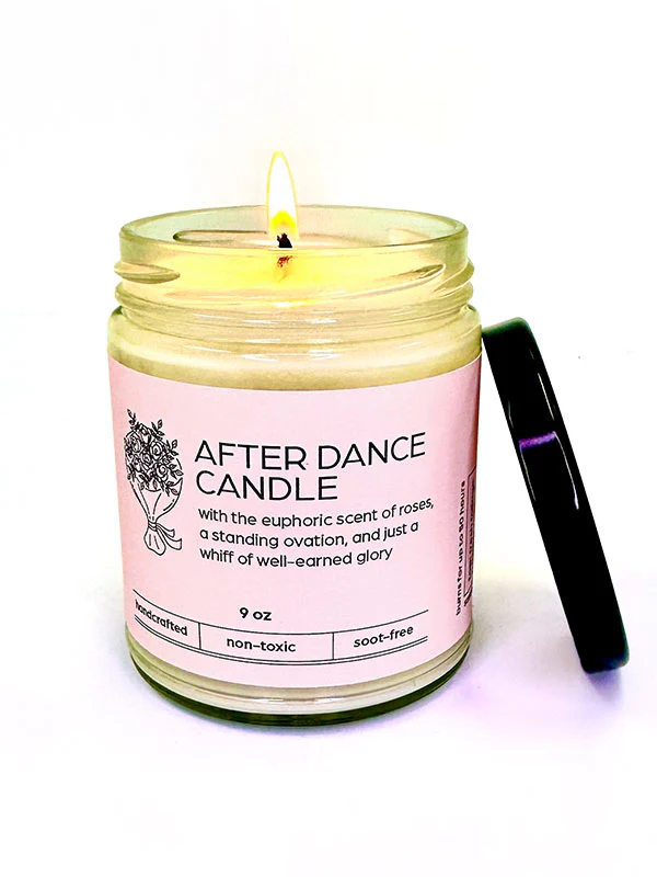 
                      
                        A lit candle with a pink label displaying "After Dance Candle" and size and scent (rose) information. A black lid leans on the side.
                      
                    