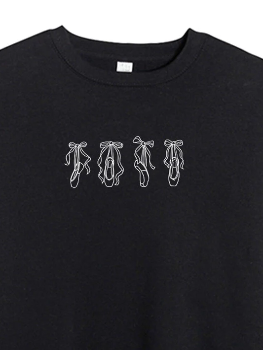 
                      
                        A close-up of the cute line art of four pointe shoes in a row with tied ribbon on a black crewneck sweater.
                      
                    