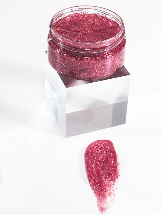 An open jar of pink sparkle gel sits on display with a smudge of the sparkle gel in front.